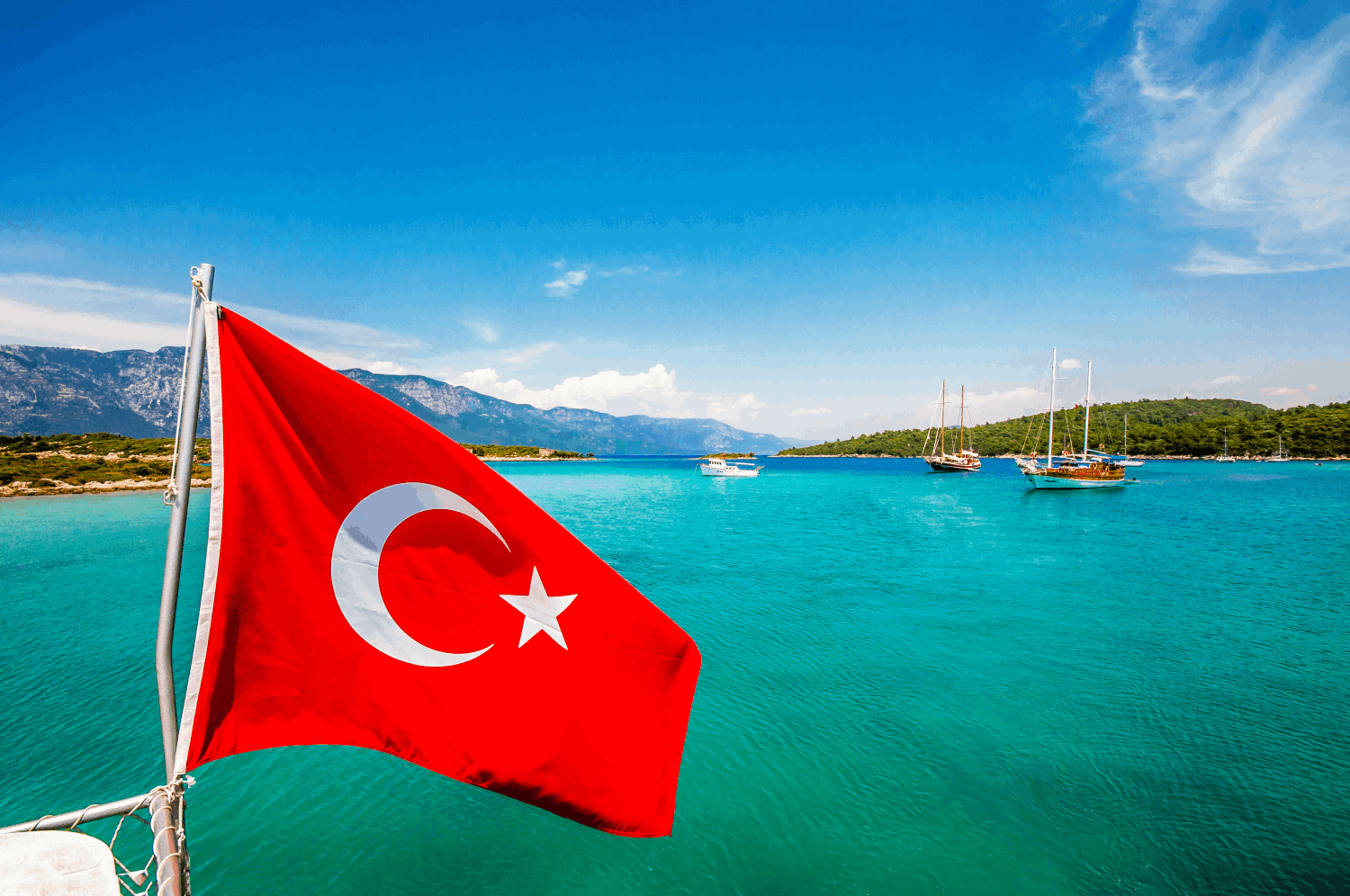 Turecká vlajka (červená s bílou hvězdou a půlměsícem) vlající před mořskou hladinou.