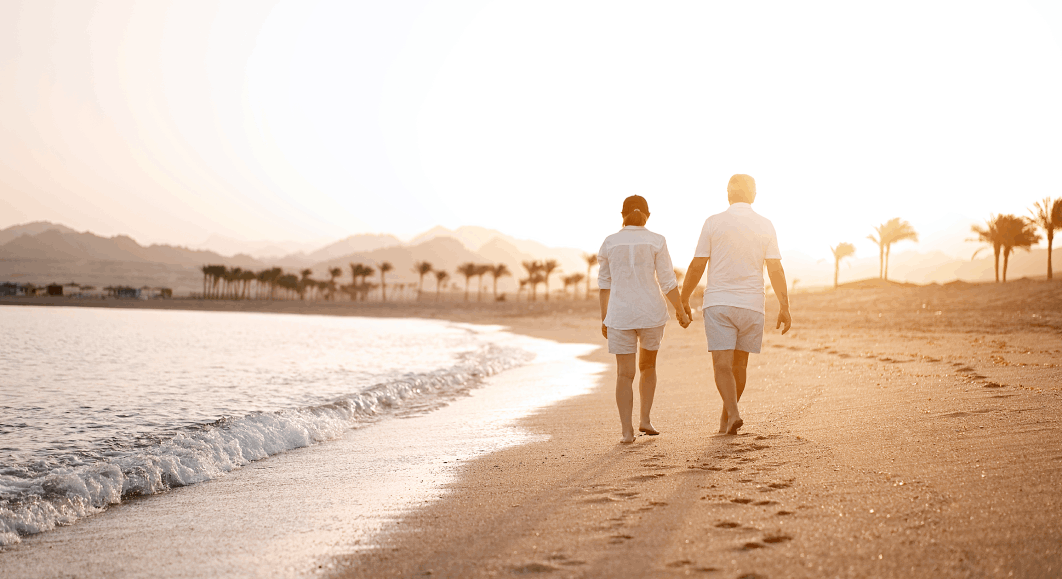 Muž a žena se drží za ruce a prochází se při západu slunce po písčitém pobřeží.